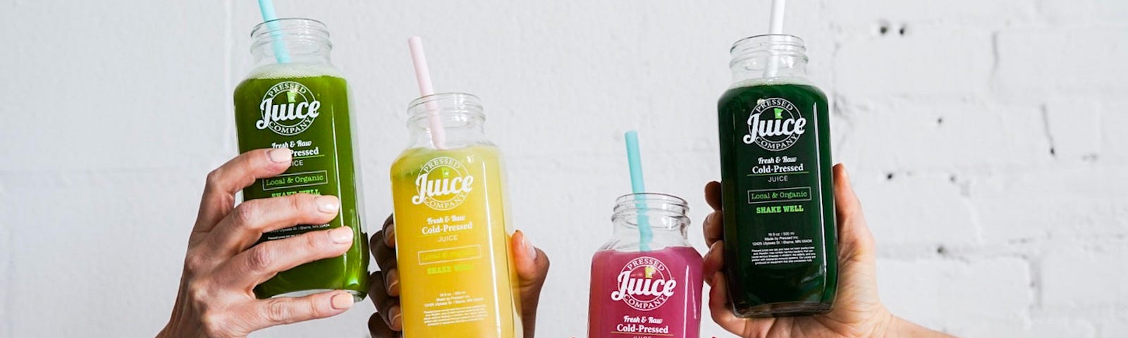 Photo of colourful juices in the cute bottles, held by hands.