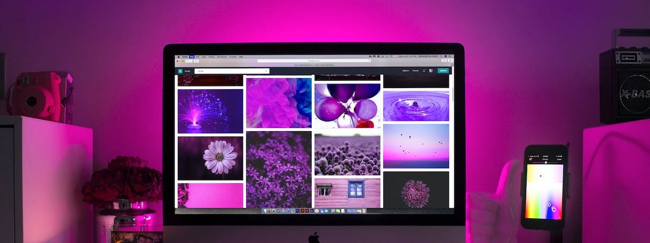 Purple lighting surrounds a computer monitor and accessories. Various purple images are on the monitor itself.