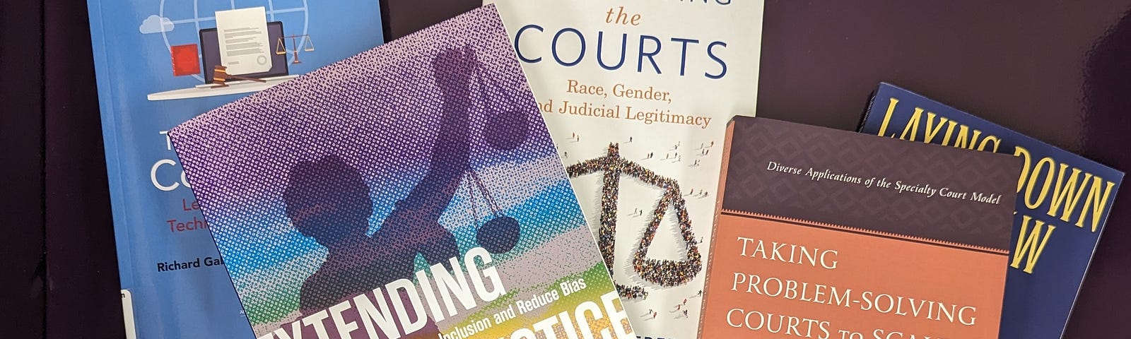 Five books are scattered over a dark purple background. One book has the title “Extending Justice” and the image on the cover is a silhouette of Lady Justice holding scales up with her left arm. There are multicolored stripes superimposed over the cover image. Another book has the title “Take Problem-Solving Courts to Scale.” It, too, has a photo of Lady Justice on the cover with books blurred in the background. The book title is printed in white text on a rust colored banner.