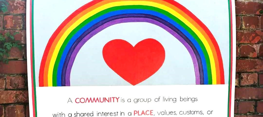 A poster shows a rainbow painted above a heart and positive words about community as a place for belonging.