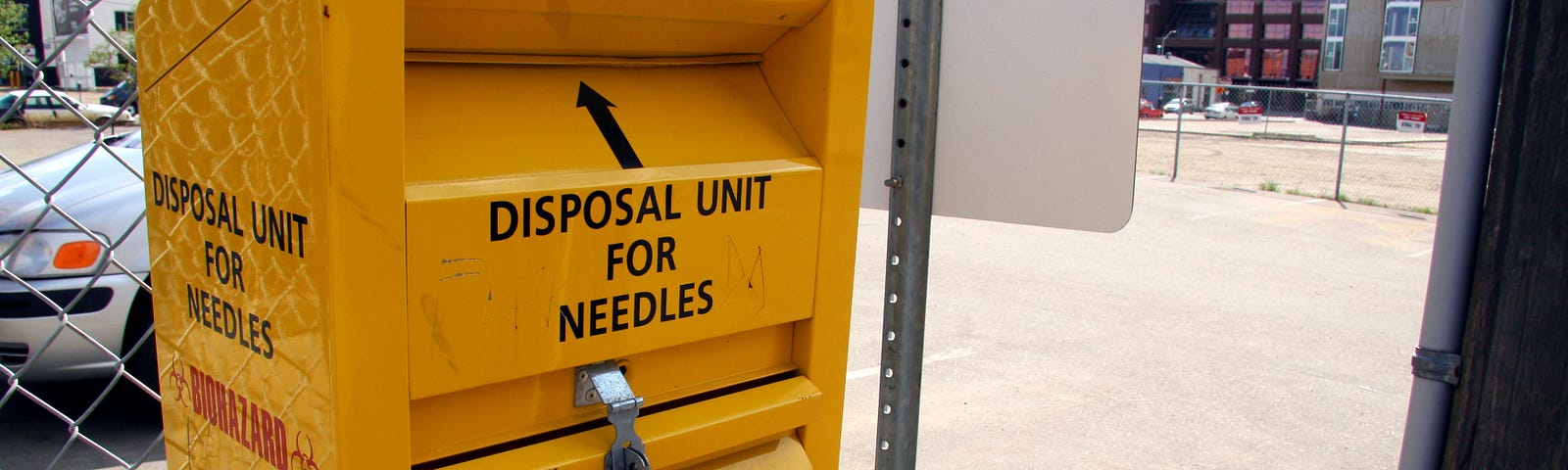 Yellow needle disposal bin on a chainlink fence