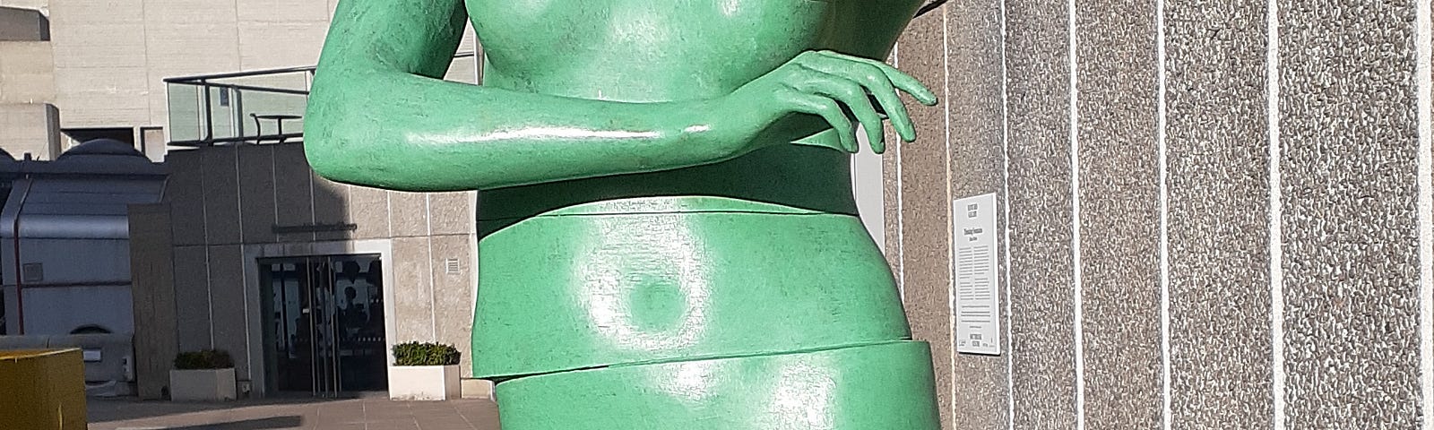 A green statue of a nude woman, arms crossed and headless