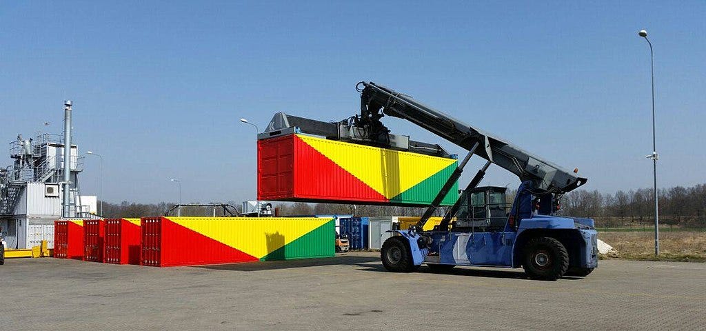 A crane lifts a container painted in red, yellow, and green, next to four identical containers.