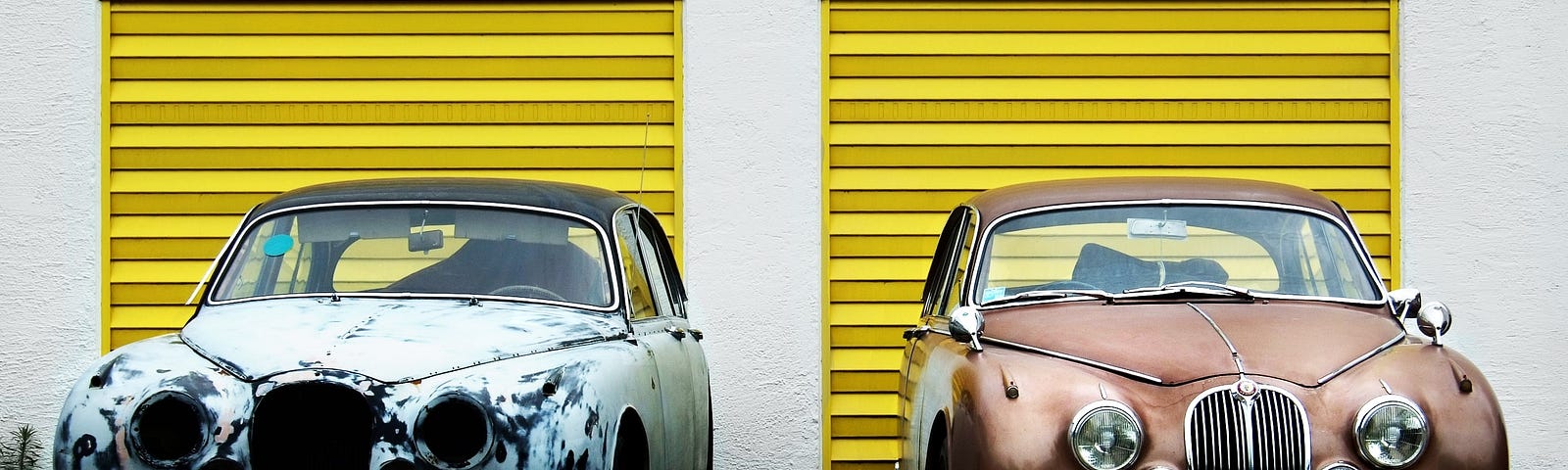 Two car side by side in front of yellow doors. Left car is old and dilapidated. Right car is a gorgeous classic.