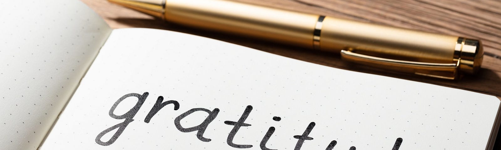 Pen and journal sit on a desk. On the journal page is written “gratitude.”