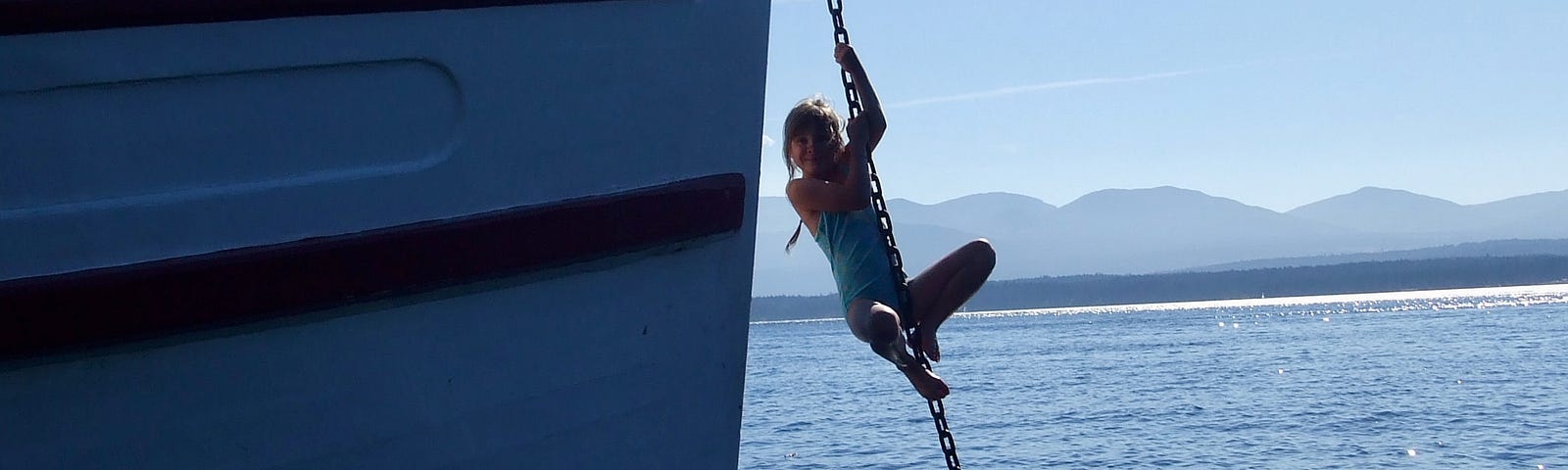 A girl climbs an anchor chain attached to a boat. A blue sky and an ocean are behind her image.
