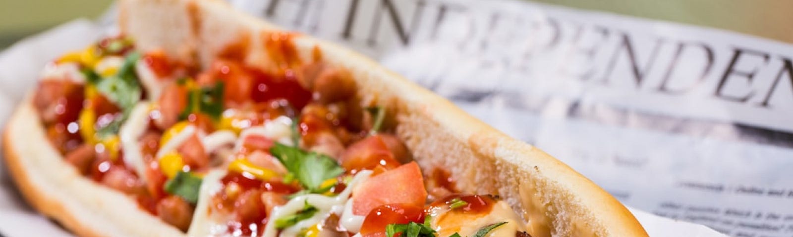 A hot dog topped with cheese, tomatoes, onions, green onions, ketchup and mustard.