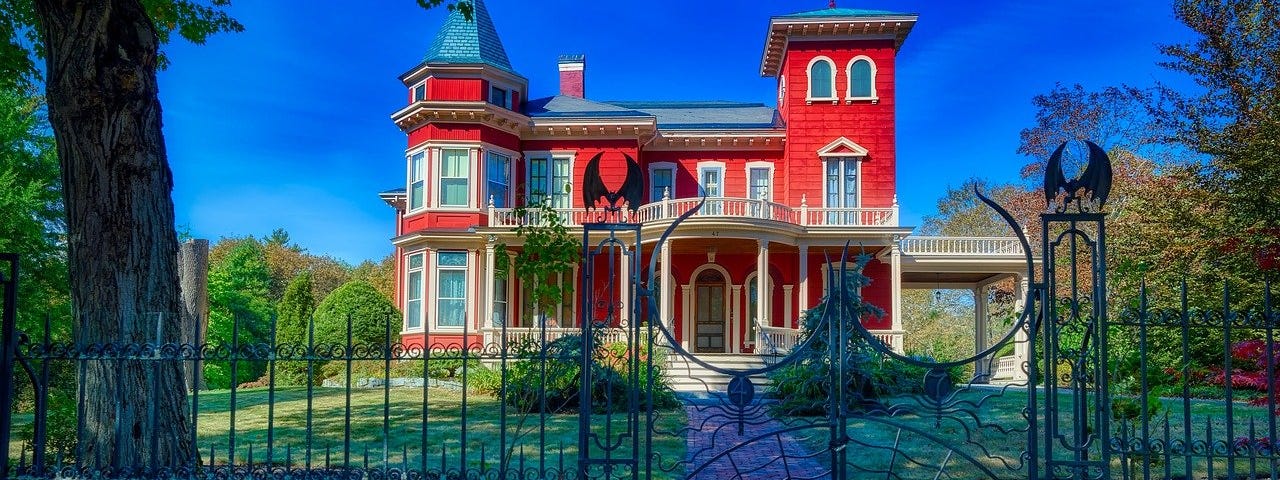 Home of Stephen King, an old Victorian-style red house surrounded by a wrought iron fence with bats, spiders, and dragons.