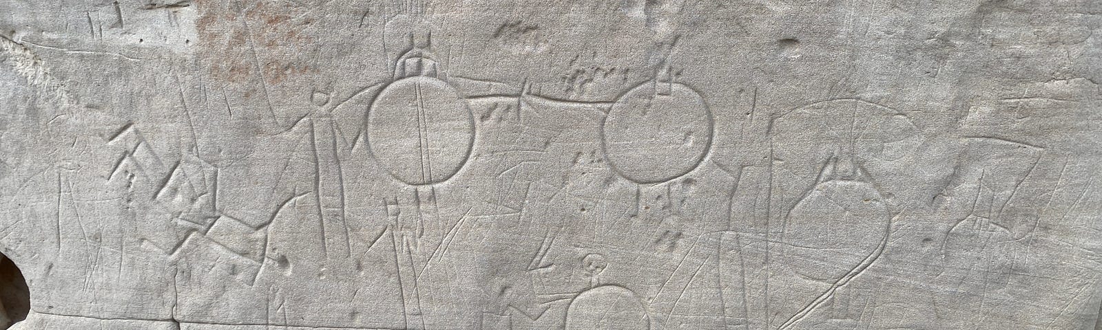 Multiple carvings of round objects with stick men standing behind them.