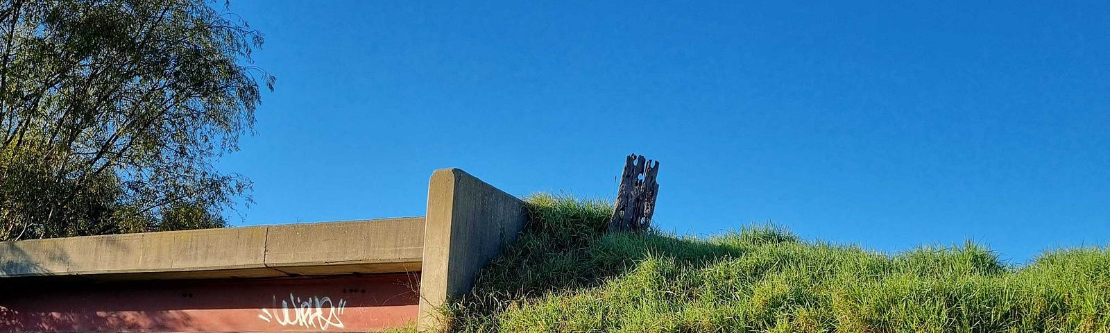 A sign saying ‘Gippsland Plains Rail Trail’ in front of a grassy hill and old rail overpass