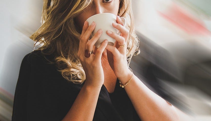 Young woman, blonde hair, drinks coffee/tea and looks surprised / alert