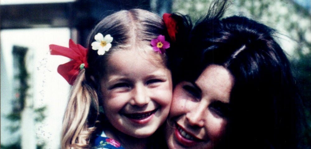 Mother hugging her young daughter who has red bows and flowers in her hair