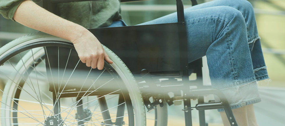 Picture of a person in a manual wheelchair. They are wearing a green shirt, blue jeans and green sneakers. Their face is not within the frame of the picture. Photo credit: Canva