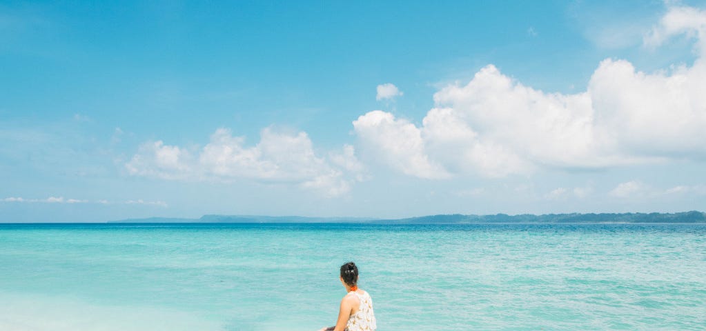 A woman sits on a tree over the water and looks out over a turquoise sea. Lessons narcissistic abuse