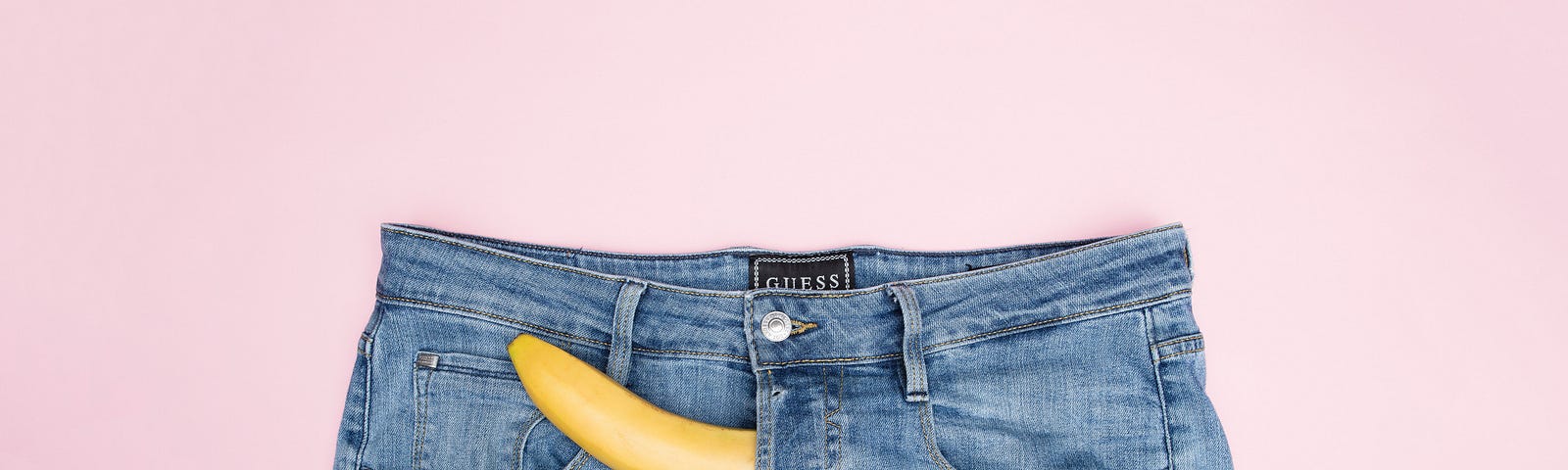 A banana poking through the flies of a pair of jeans.