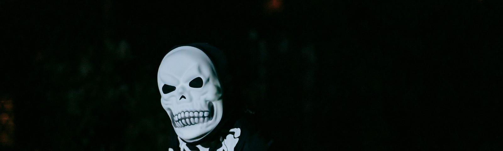 Anonymous child in skeleton mask against dark background.