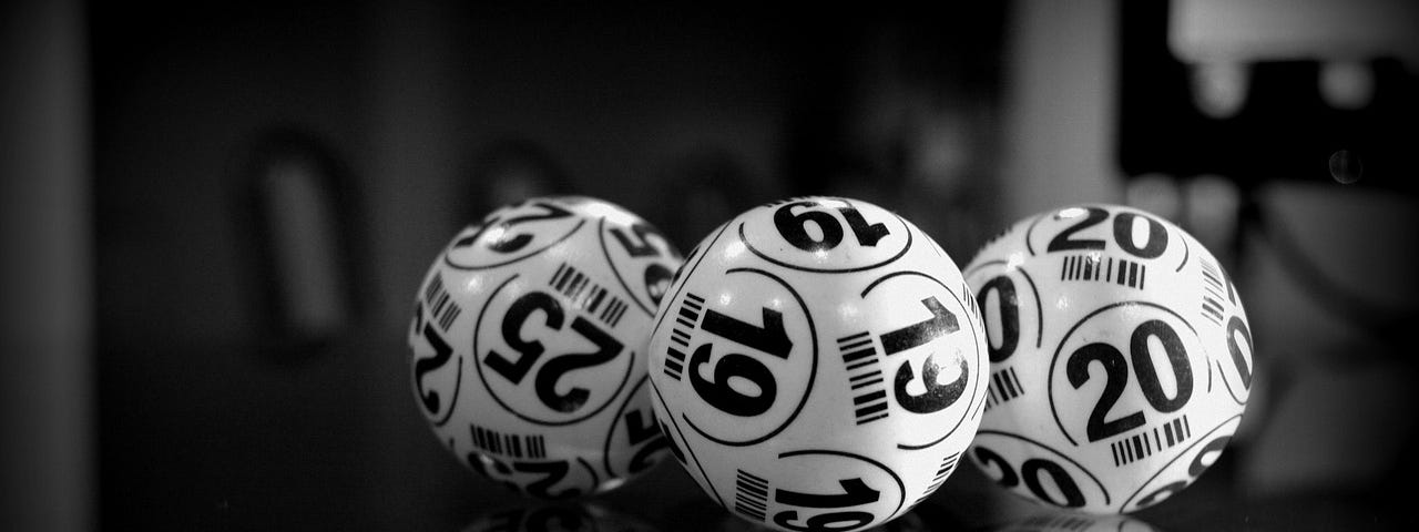 Monochrome image with black background and surface and three white bingo balls on the surface.