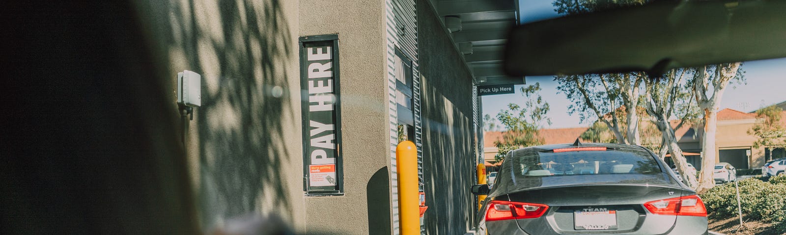 Veiwed from the rear seat. We see a women waiting in line at a drive thru resturant. The caption below reads “Get used to the view it’s probably going to cost you your job.” (Credit https://www.pexels.com/@rodnae-prod/)