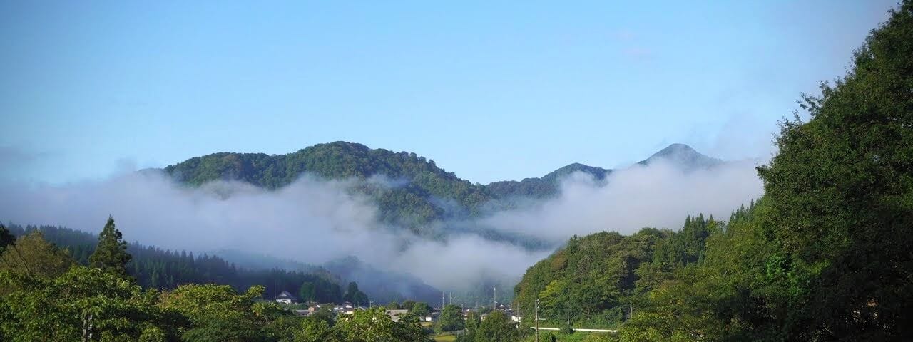 Road in the foreground leads to a mountain shrouded in morning fog over the village of Sekigawa at the base of Mt. Maya in Tsuruoka, Yamagata Prefecture.