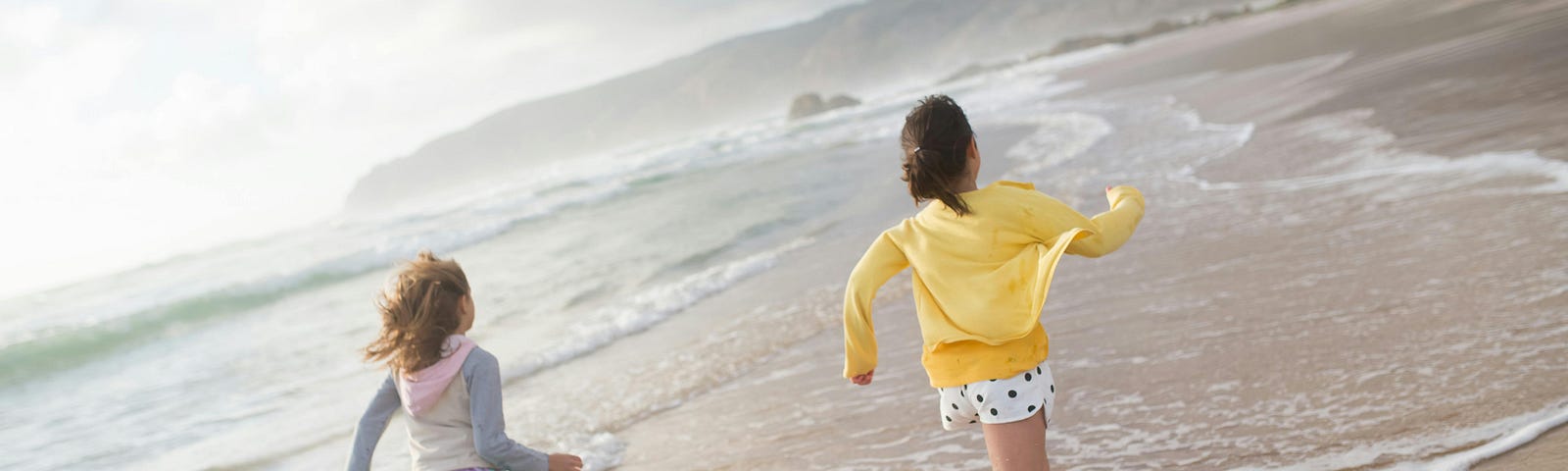 Two young girls race along the beach in the surf.