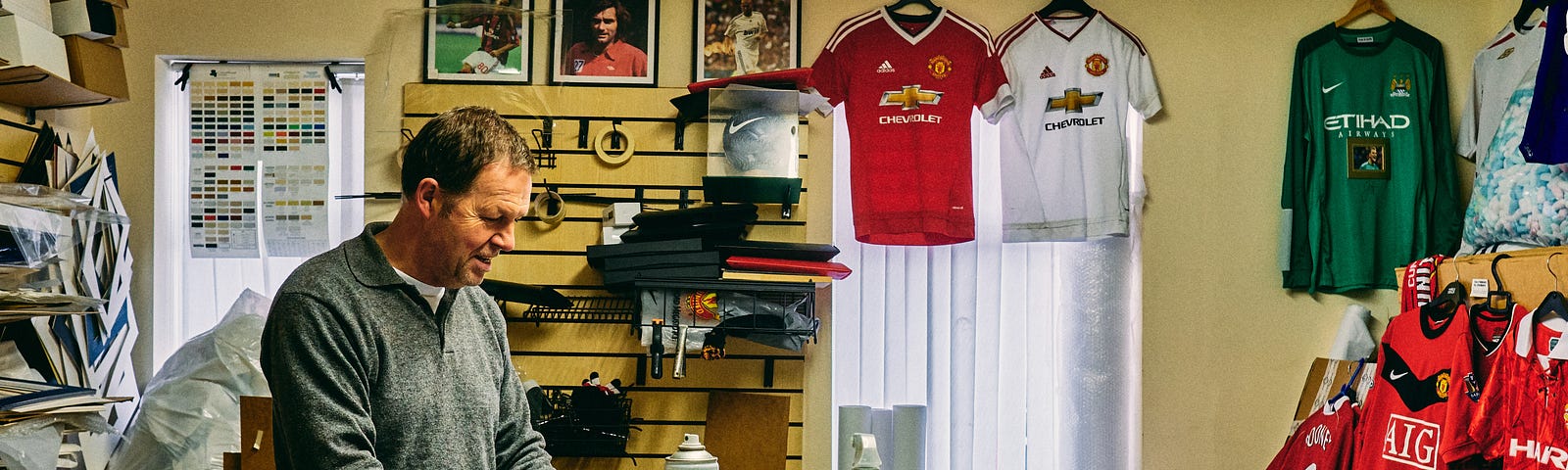 Man Smiling in Cluttered Room with Football T-Shirts on the Wall