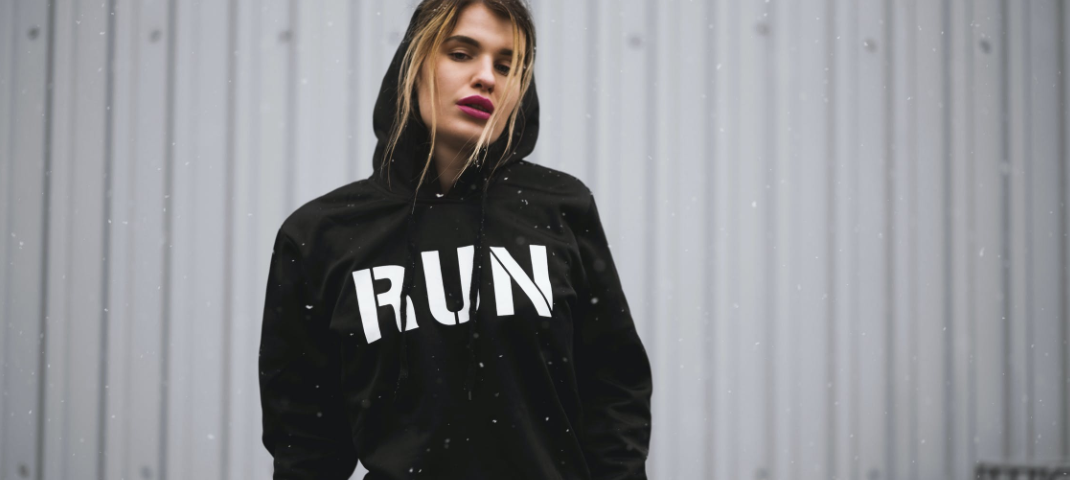 A fatigued woman wearing black hoodie, with the word “RUN” emblazoned across her chest.
