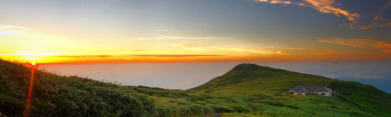 The sun sets over the Ninth Station of Mt. Gassan with Mt. Chokai poking its head through the cloud above the mountain hut