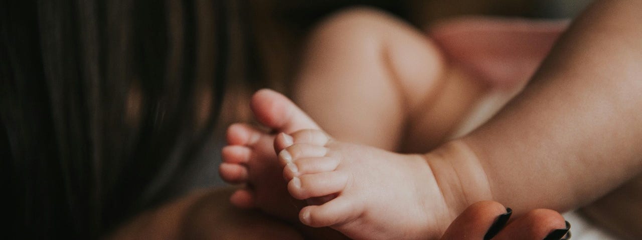 A mother’s hand gently holds her baby’s tiny feet, symbolizing love and care.