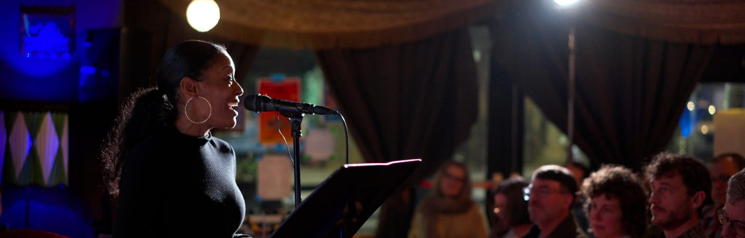 A photo of a journalist talking into a microphone to an audience of people.