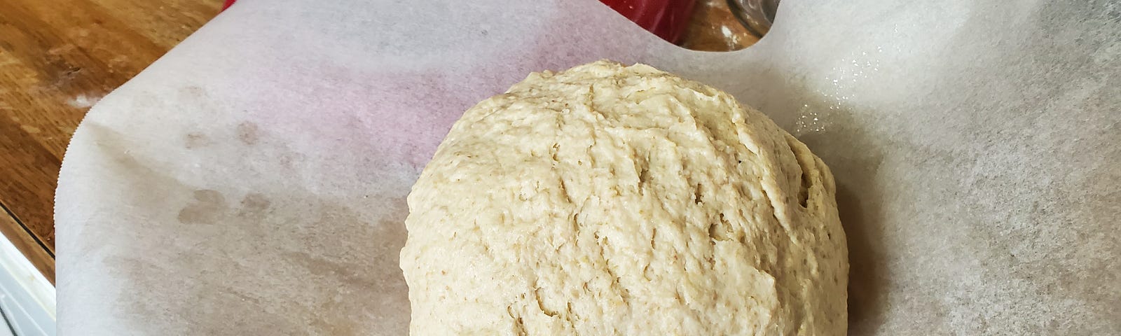 Loaf of gluten free bread dough resting on a sheet of parchment paper.