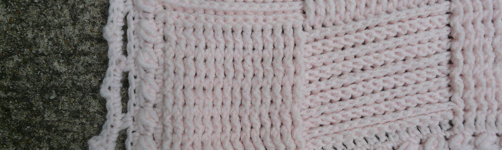 A pink crochet blanket worked in a textured basketweave stitch