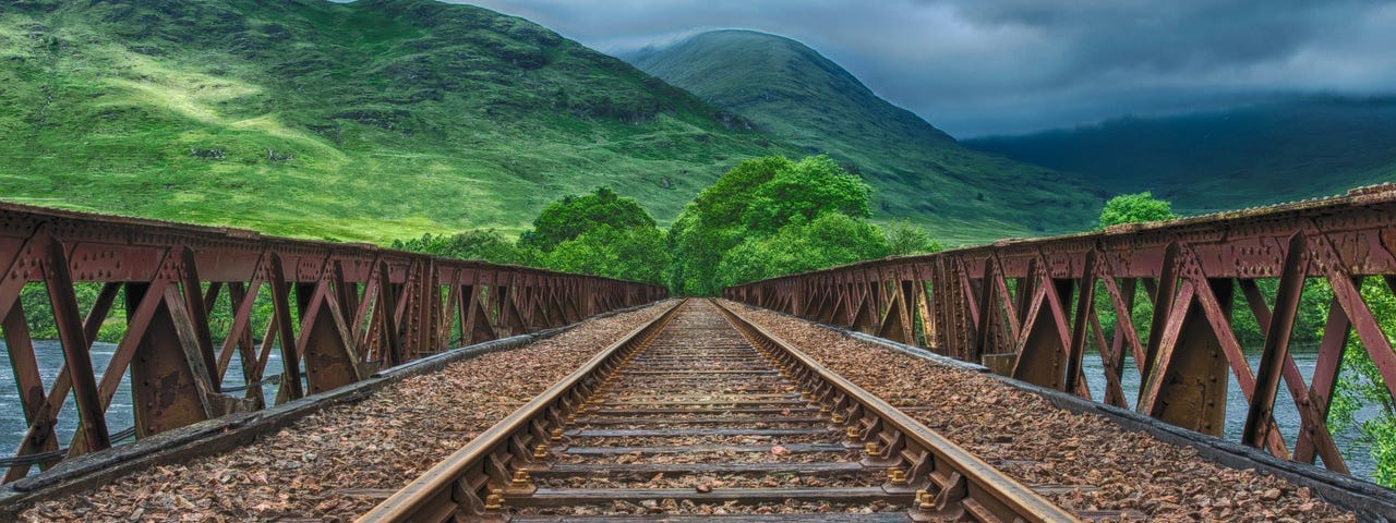 Image: Railroad tracks leading toward green hills.