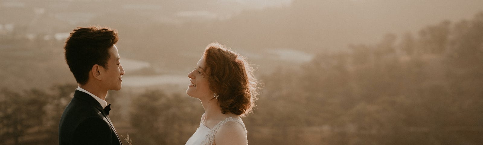 Groom and bride stand holding hands with a bouquet at the top of a mountain, overlooking a pretty vista.