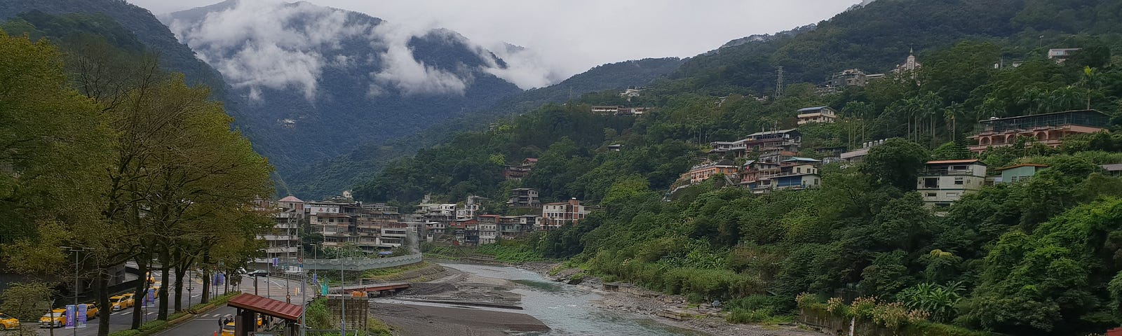 Tourist buses line up along the river’s edge overlooking the mountains and some houses.
