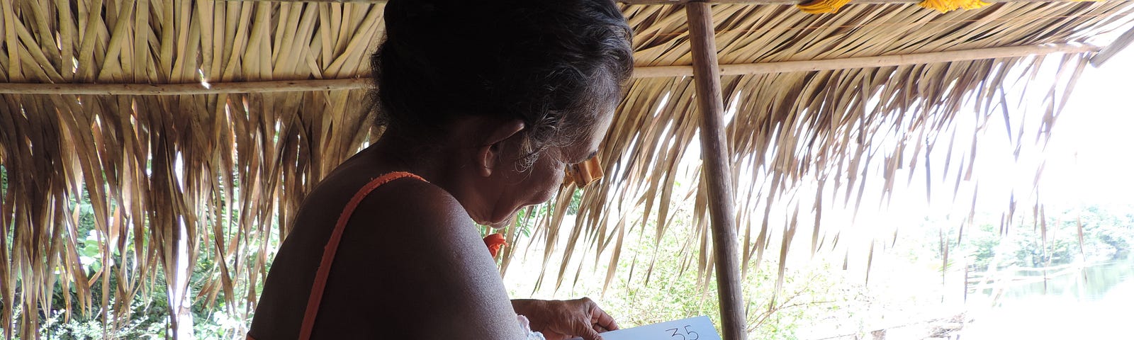 A woman sitting under a thatched roof viewing a photo of a fish