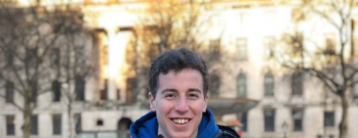 Man with brown hair wearing a jacket standing outside in front of a building in winter.