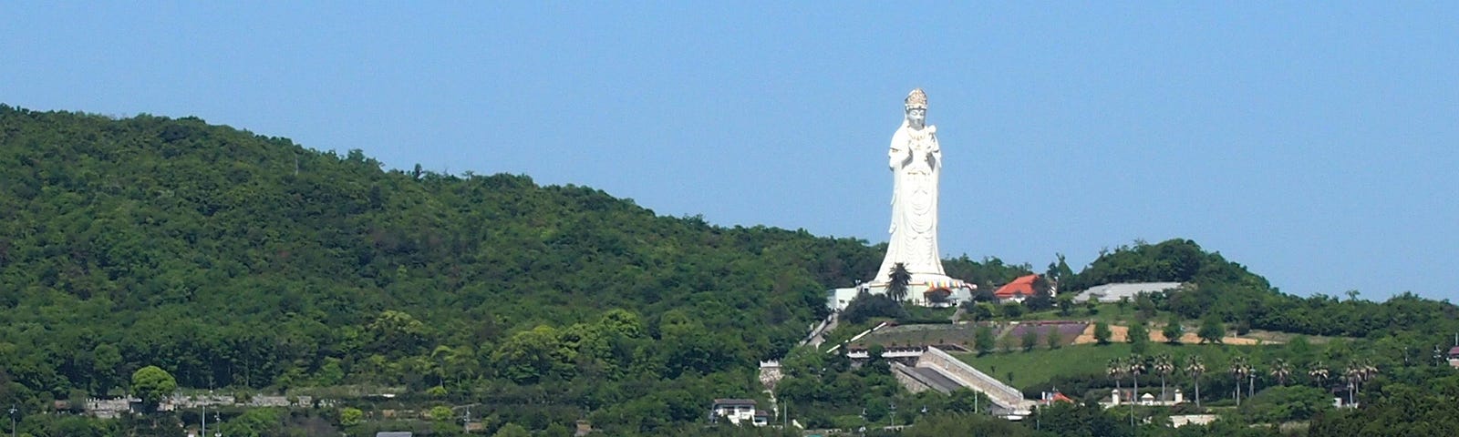 Large white Kannon statue in Japan on a hillside in the distance