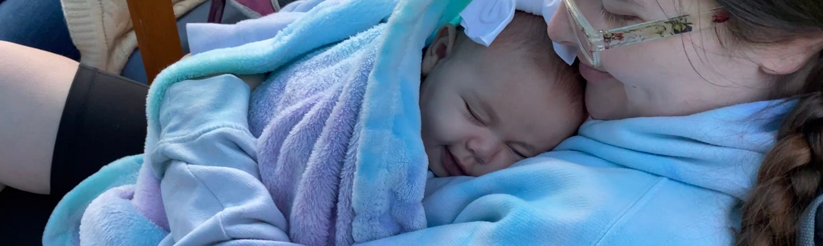A mother smiling looking down at a smiling sleeping babe wrapped in a blanket.