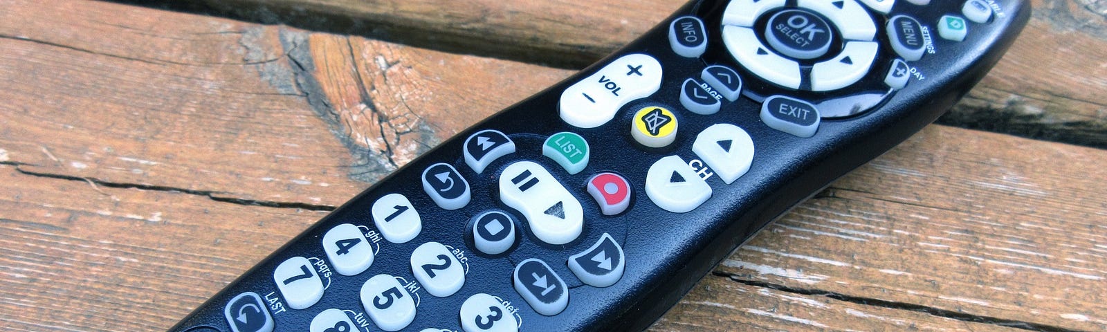 A modern TV remote control sitting diagonally across rough wooden boards.