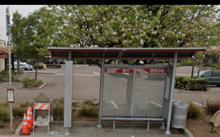 Silver San Diego MTS bus stop. Orange & white cones & construction A-frame to the left. Brown & grey sidewalk in front.