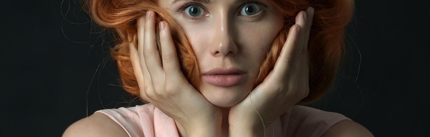 portrait of red haired woman with hands on face and a look of disbelief