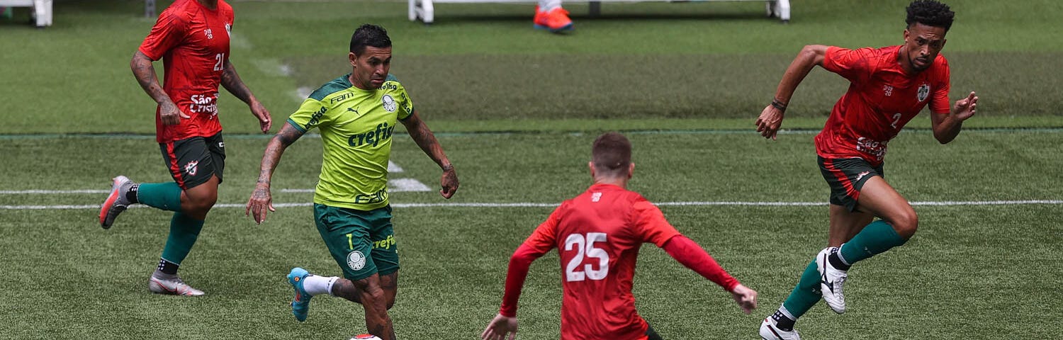 Dudu conduz a bola cercado por três jogadores da Portuguesa durante jogo-treino. Ele veste uniforme de treino do Palmeiras: camisa verde limão, calção verde e meia branca. Os jogadores da Portuguesa usam camisa vermelha com calções e meias em verde escuro