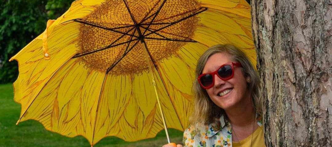 This shows a woman with a yellow umbrella by a tree.