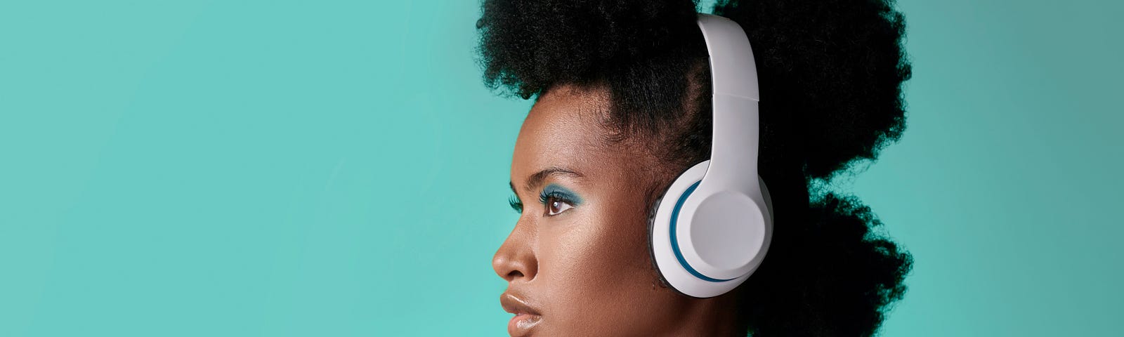 A woman listening to headphones in front of a teal wall.