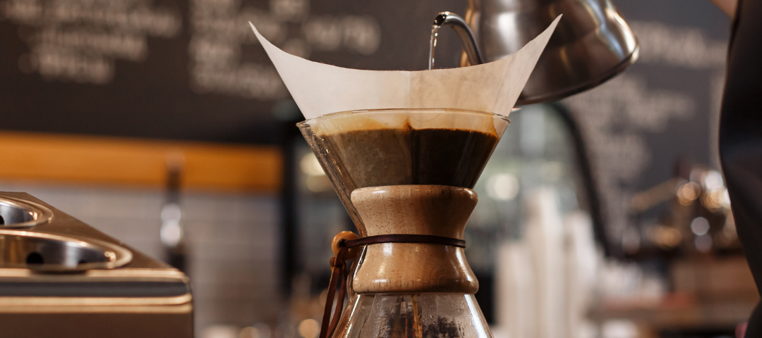 A barista pour hot water into a Chemex coffee brewer to make fresh, great-tasting coffee.