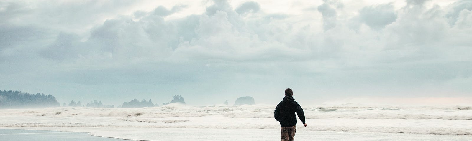 Man running on beach into waves, soft blue grey tones.