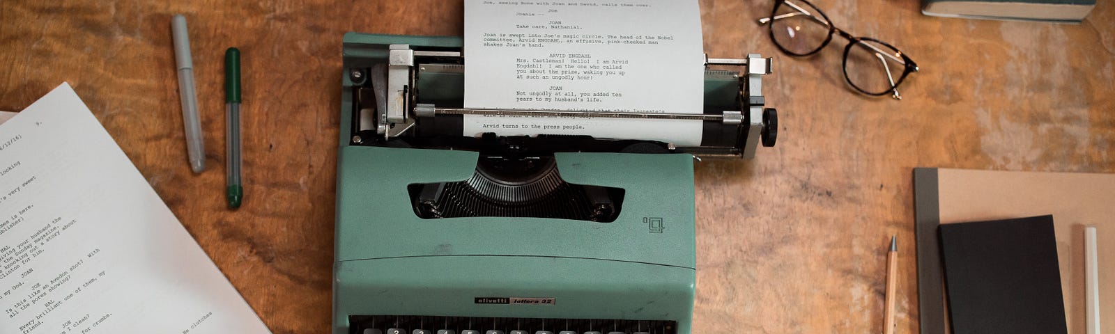 A person typing on a green typewriter on a brown wooden table