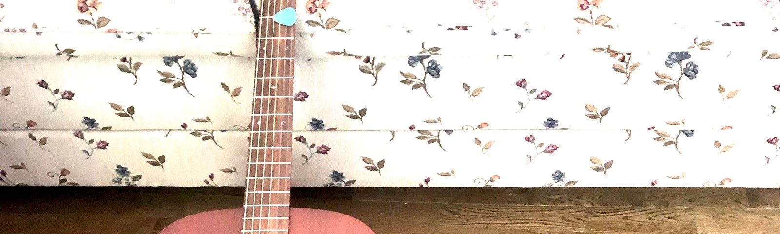 A picture of a mahogany wood acoustic Martin guitar, lying on a couch with a floral pattern. There’s a MacBook laptop opened up with the screen facing the other way.