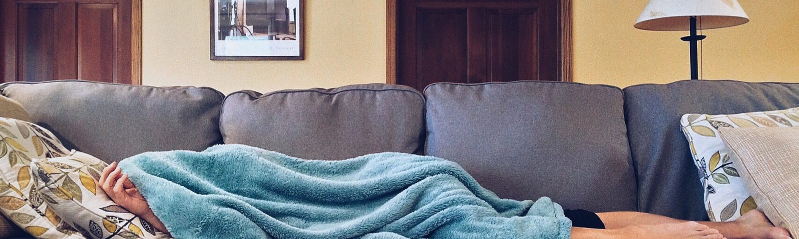 Photo of person laying on the couch covered in a blanket.