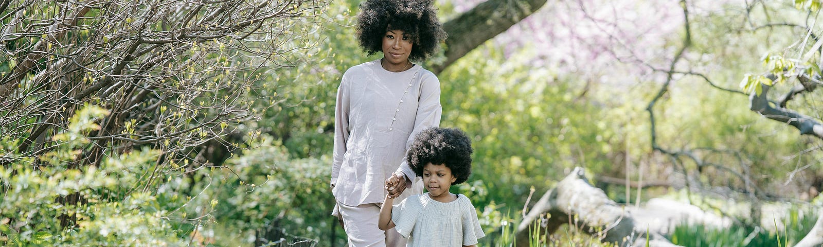 A Black woman, and her daughter, hold hands as they walk on a path at a park.
